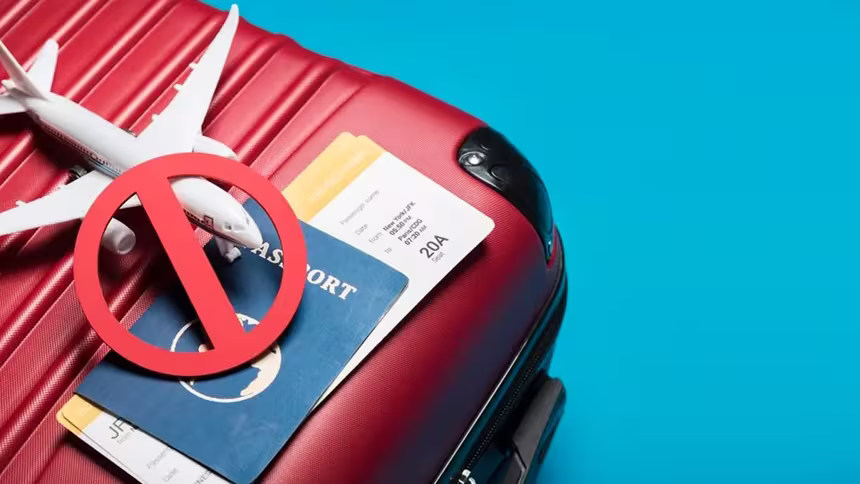 Passport, plane tickets, and a toy plane weighed down by a stop symbol on top of a suitcase, representative of the dangers of travel fraud scams